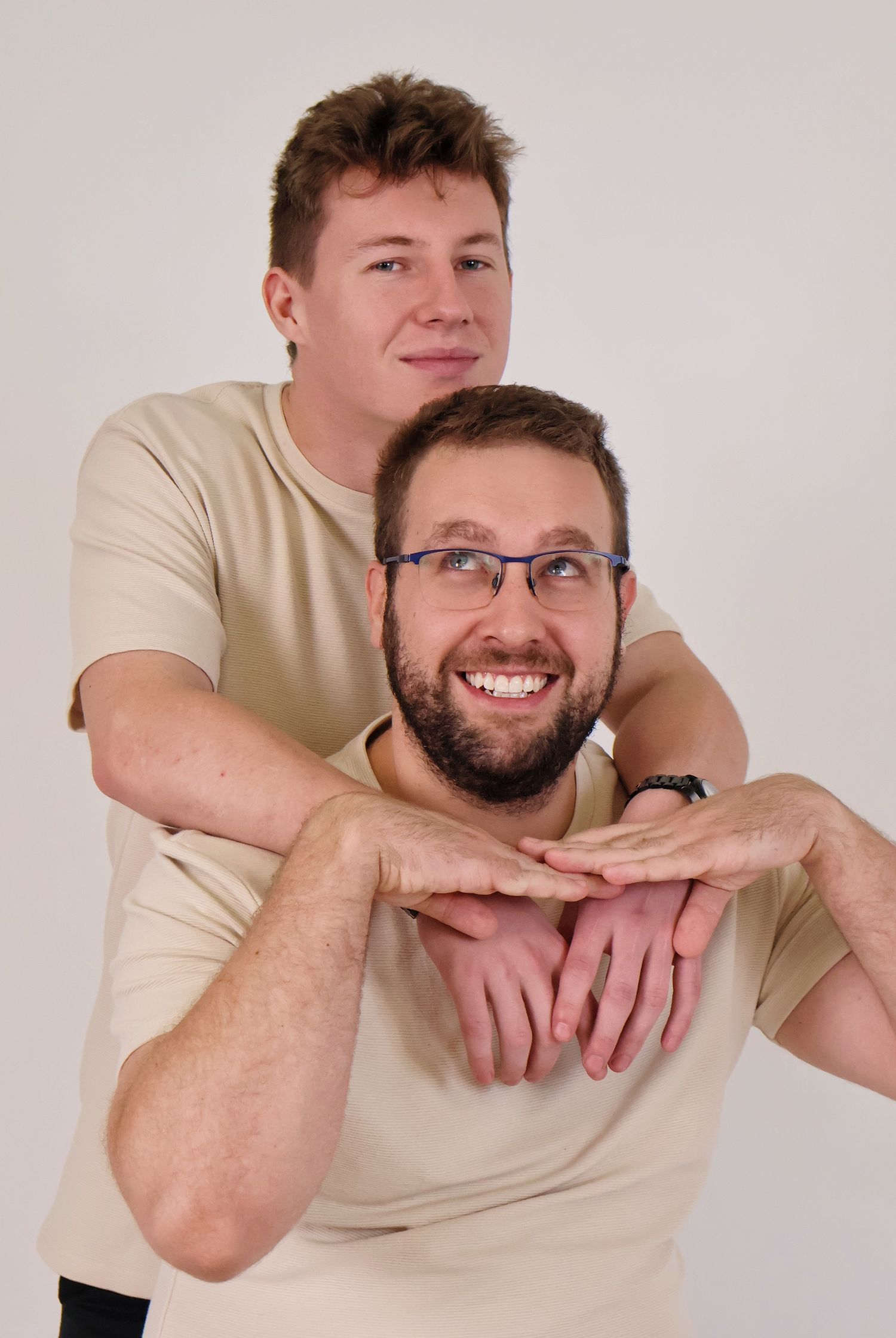 Two men posing playfully in matching beige t-shirts against white background in studio portrait.