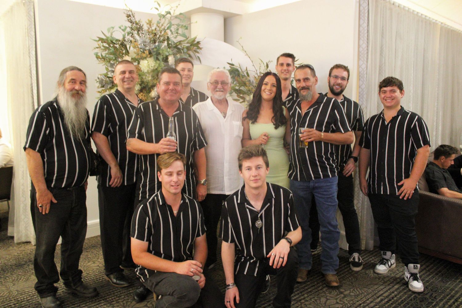 Large group photo with men in black striped shirts surrounding a couple at a celebration.