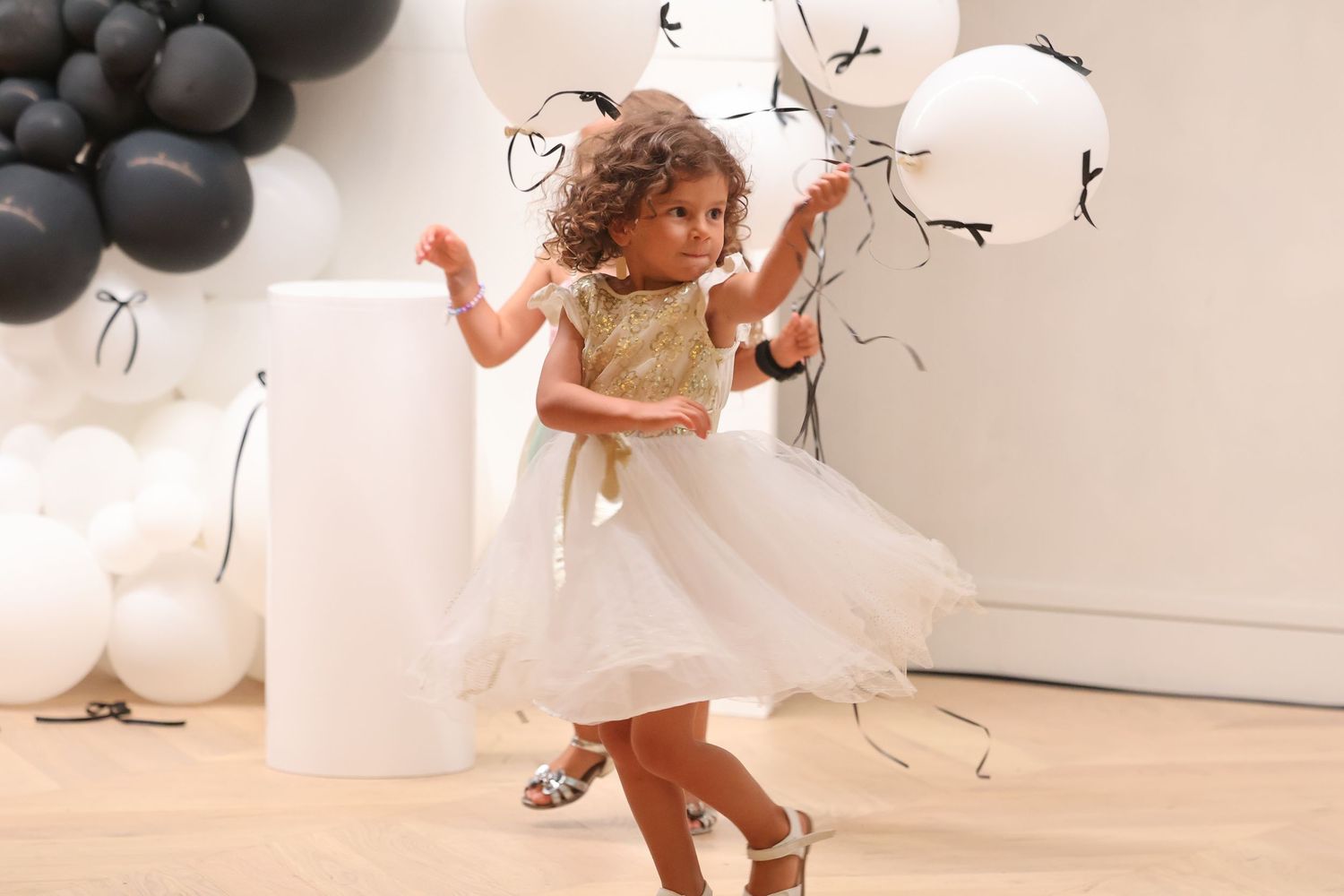 Young girl in white tutu dress dancing with balloons at a birthday party celebration.