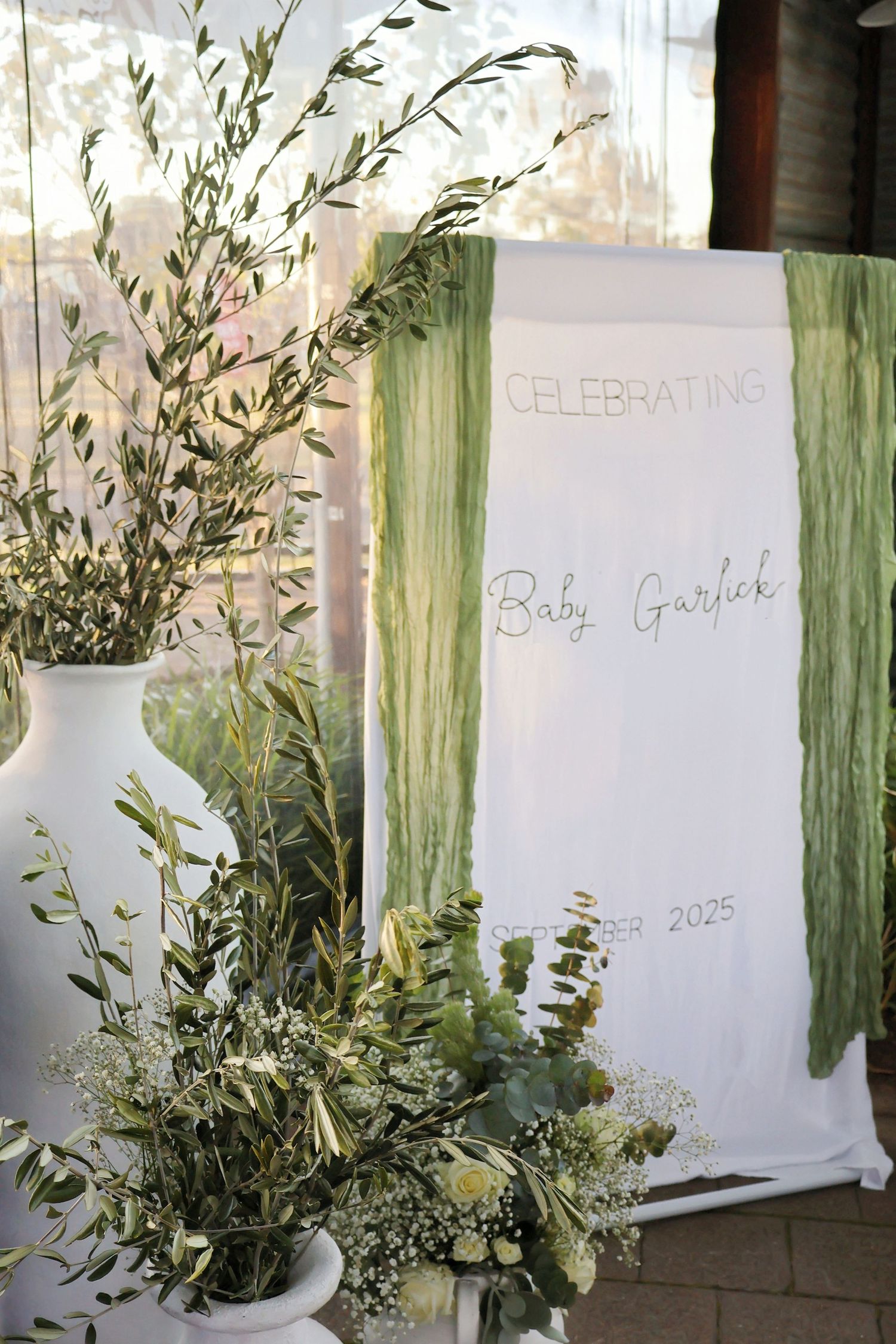 Elegant baby shower backdrop with green botanical decor celebrating Baby Garlok 2025.