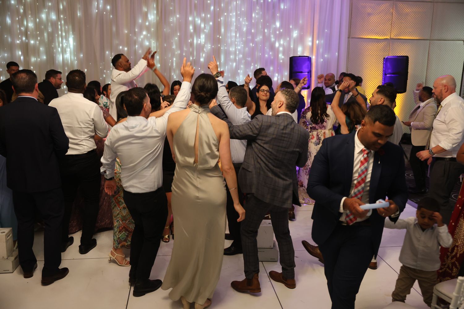 Guests dancing joyfully on white dance floor at lively wedding reception party.