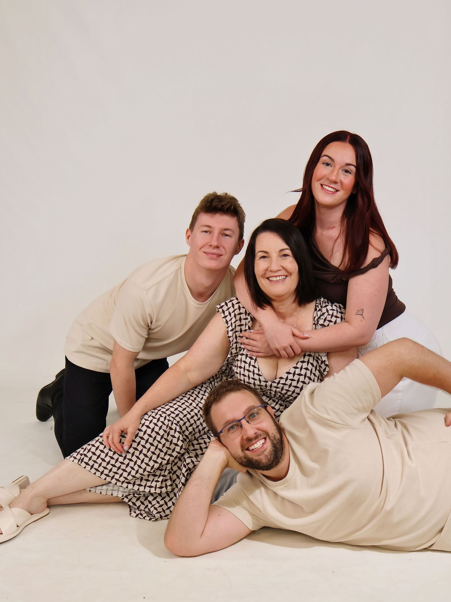 Family of four posing playfully together on the floor in a bright white photography studio.