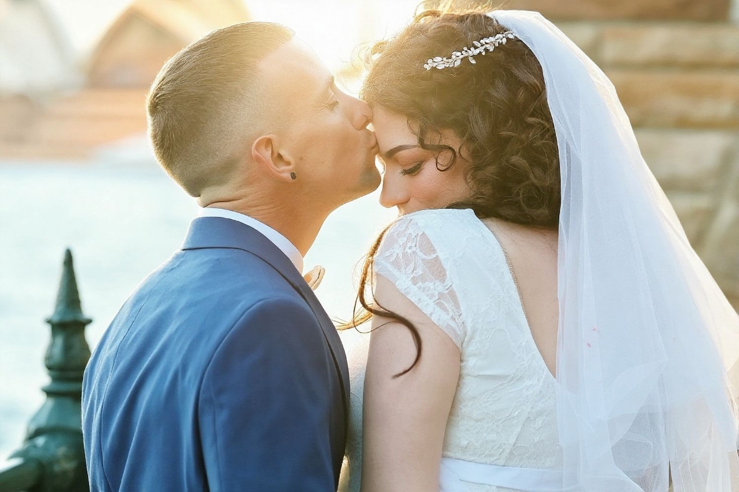 Bride and groom sharing a romantic kiss on their wedding day, bride wearing white lace gown and veil.