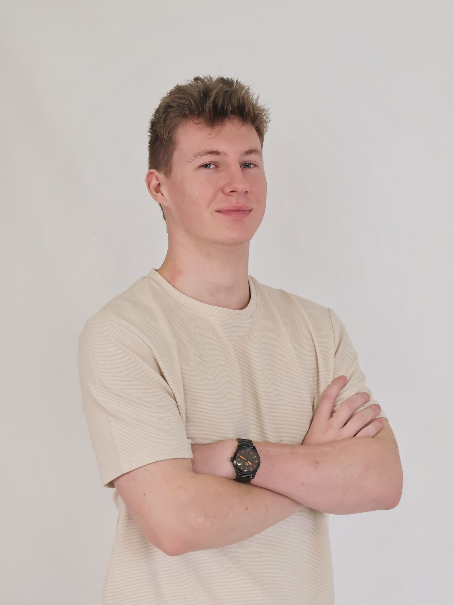 Confident young man in beige t-shirt with arms crossed posing against a clean white background.