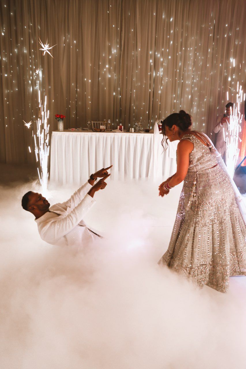 Bride and groom share dramatic first dance surrounded by dry ice fog and sparkling fireworks indoors.