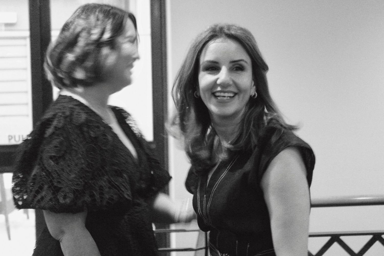 Two elegantly dressed women smiling and conversing at a formal black and white event.