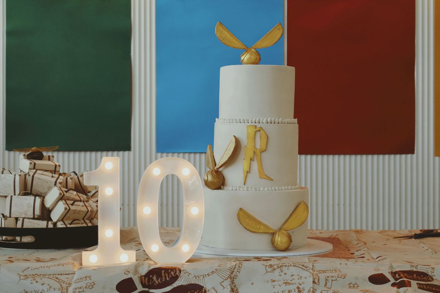 White two-tier Harry Potter birthday cake with Golden Snitch beside illuminated number 10.