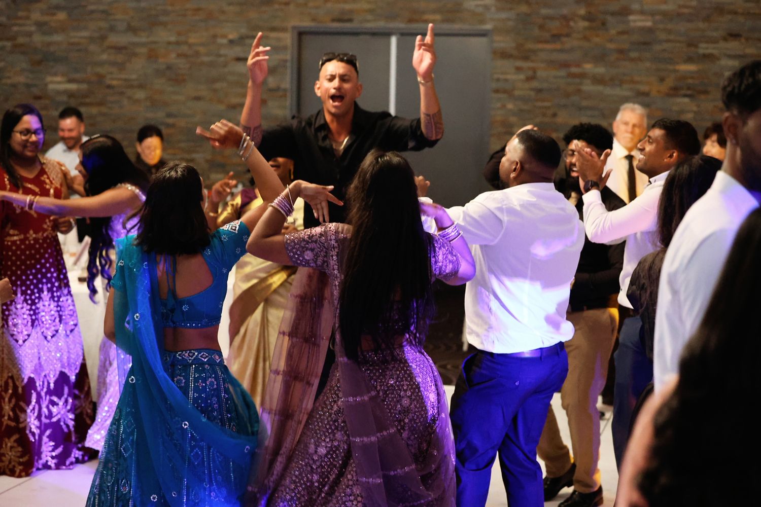 Guests dancing energetically together at a multicultural wedding reception celebration.