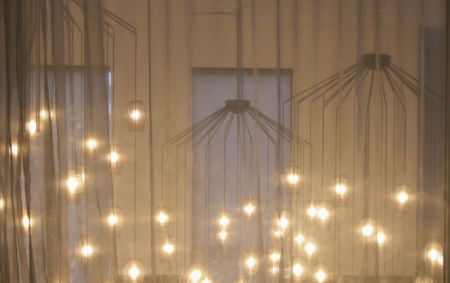 Warm glowing fairy lights hanging from ceiling through sheer curtains creating a magical atmospheric lighting display.