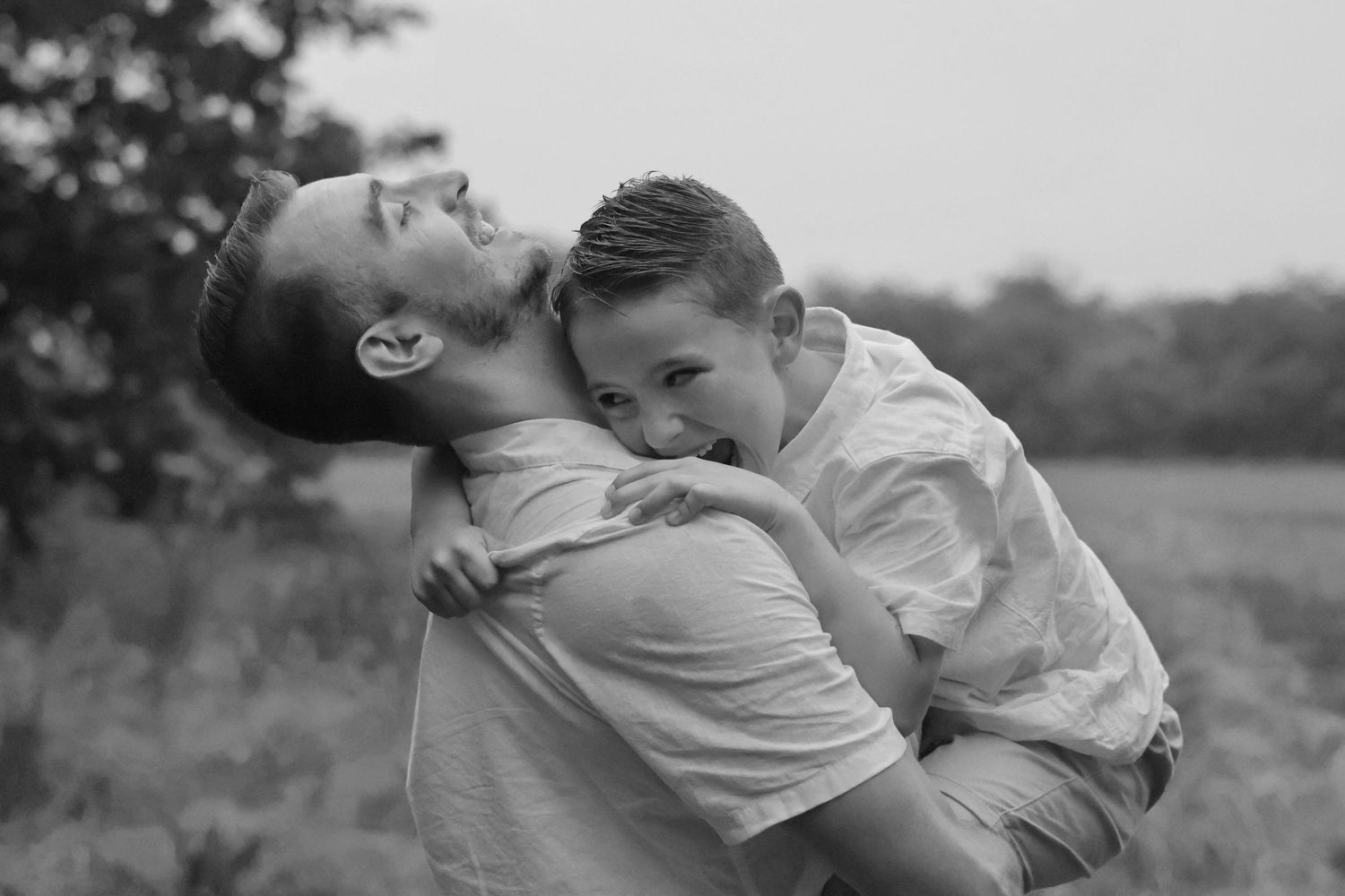 Black and white photo of a father and young son sharing a joyful embrace outdoors.
