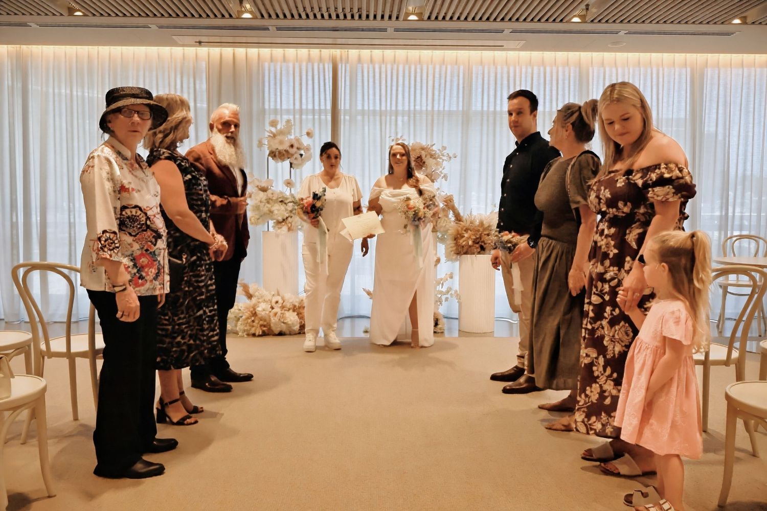 Two brides standing at altar surrounded by small group of guests at intimate wedding ceremony.