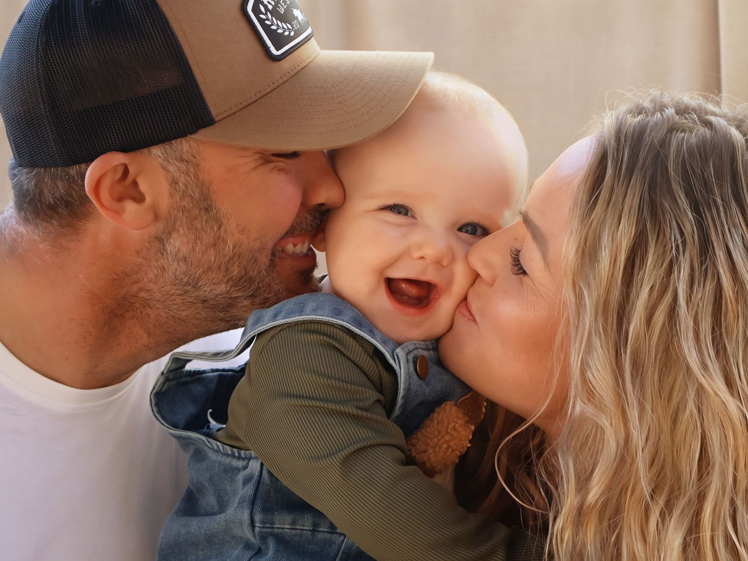 Happy parents kissing smiling baby boy on cheeks in sweet family portrait.