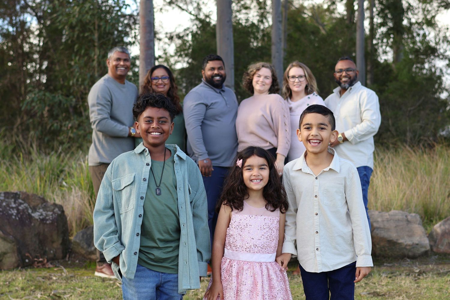 Large multigenerational family portrait outdoors with children smiling in foreground.