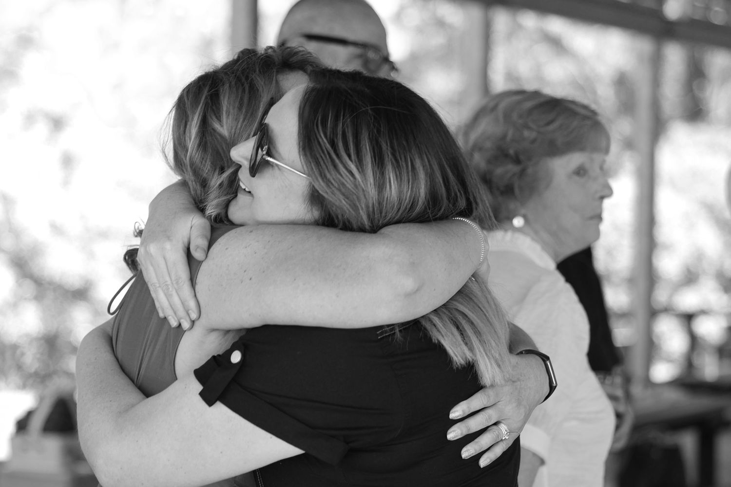 Black and white candid photo of two women sharing an emotional embrace at an outdoor event.