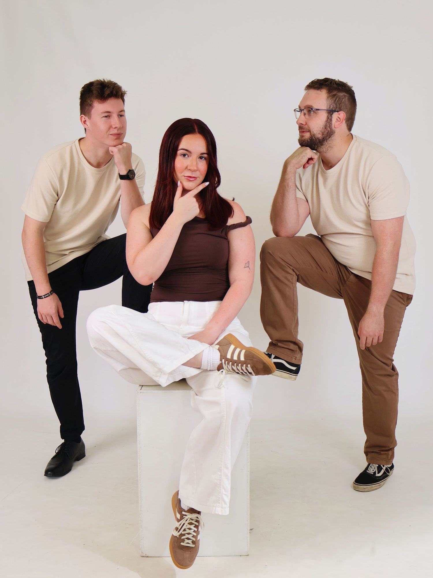 Three young adults strike a fun thinking pose together in a bright white photography studio.