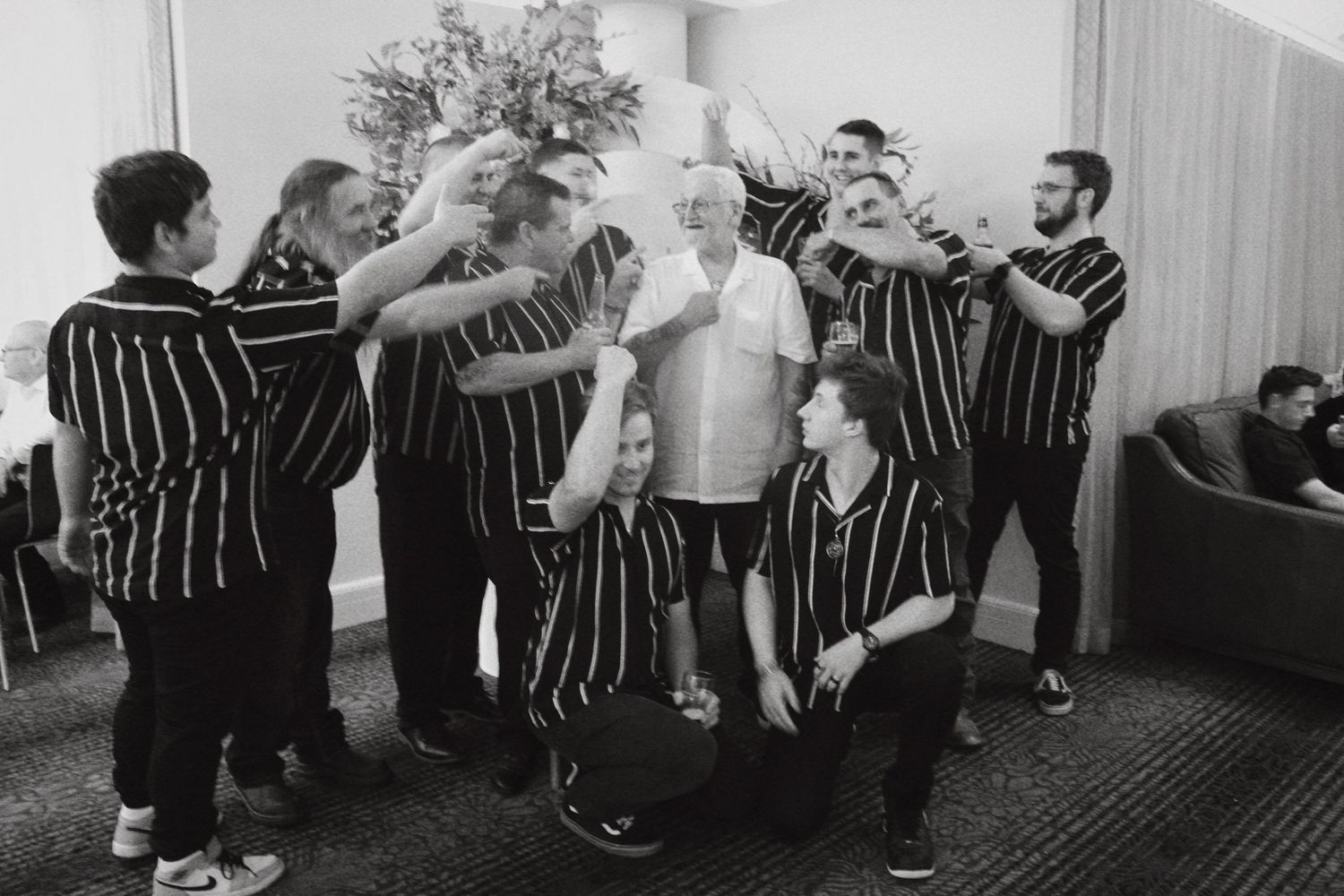 Group of men in striped uniforms toasting with an older gentleman at a party.