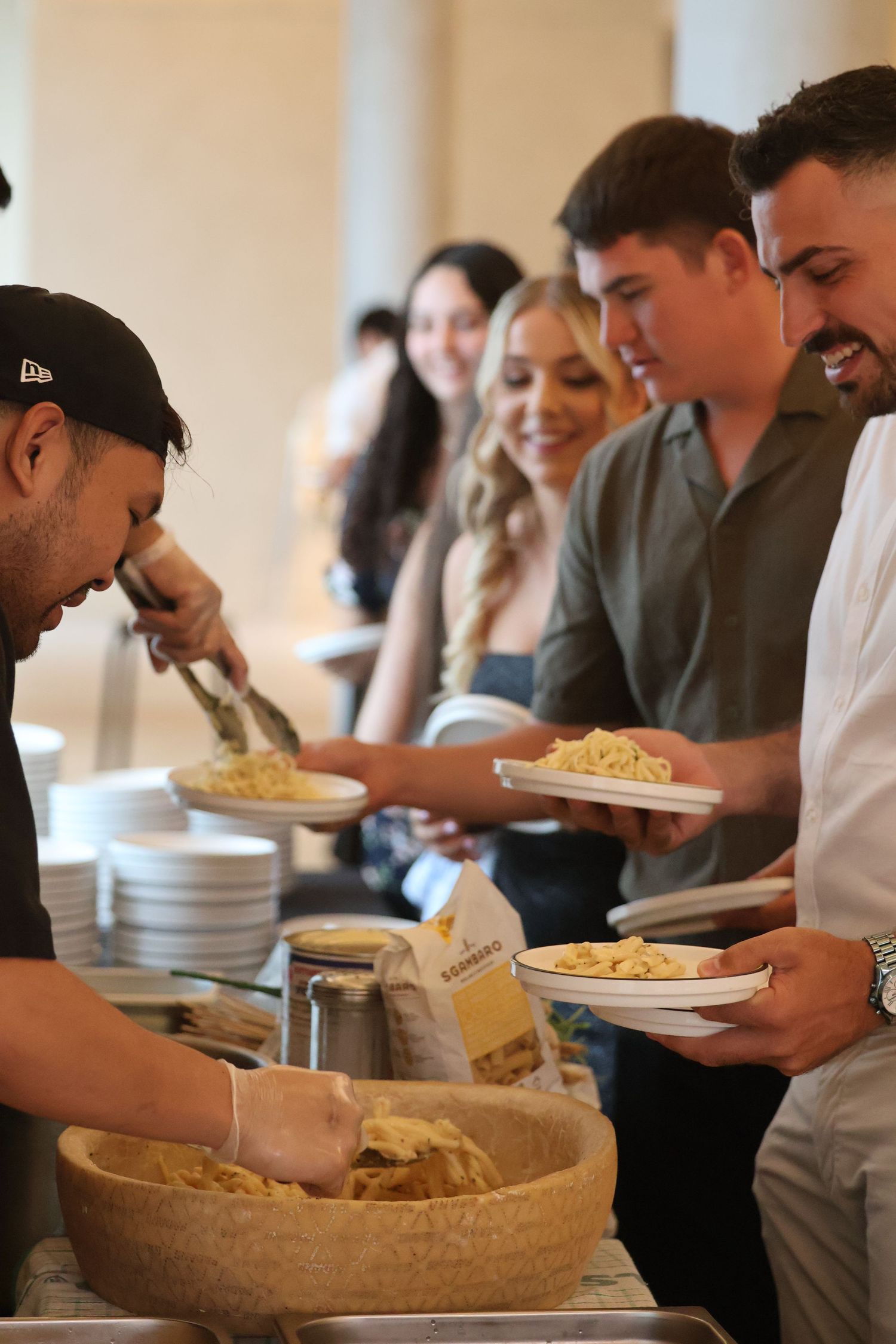 Chef serving fresh pasta to guests at a buffet line during an Italian catered event.