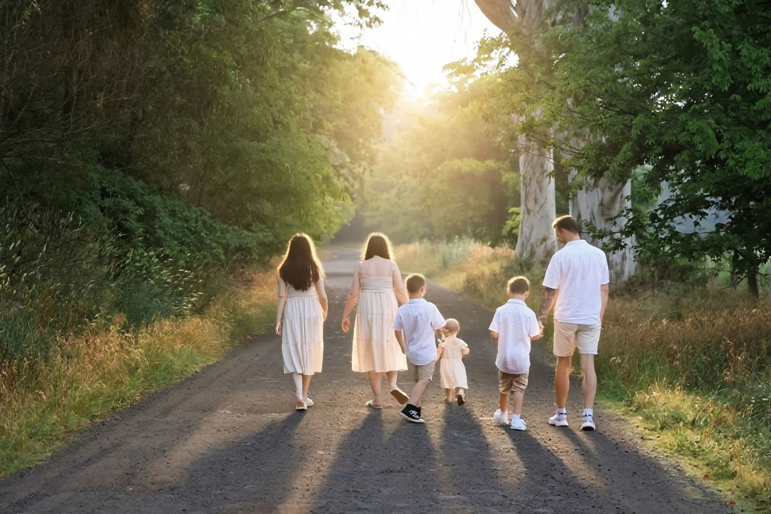 Family of five walking away down a sunlit country road surrounded by golden trees and lush greenery.