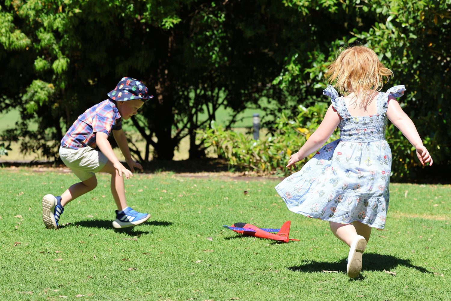 Two young children playing on green grass outdoors, with a colorful toy rocket on the lawn.