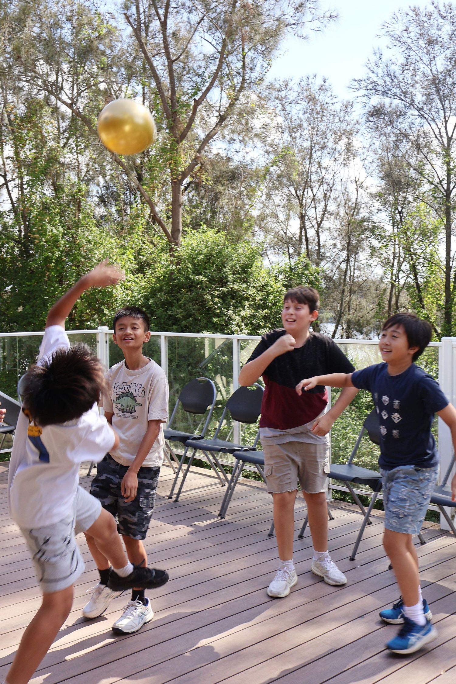 Four boys playing with a golden balloon snitch on a sunny outdoor wooden deck.