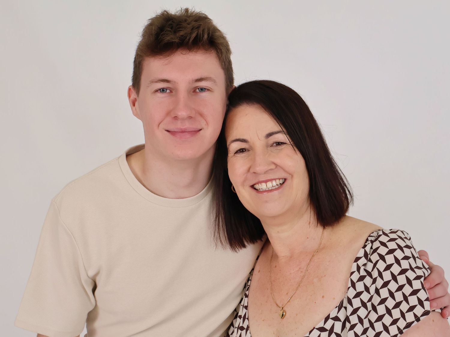 Young man and older woman smiling together in warm close-up portrait against white background.