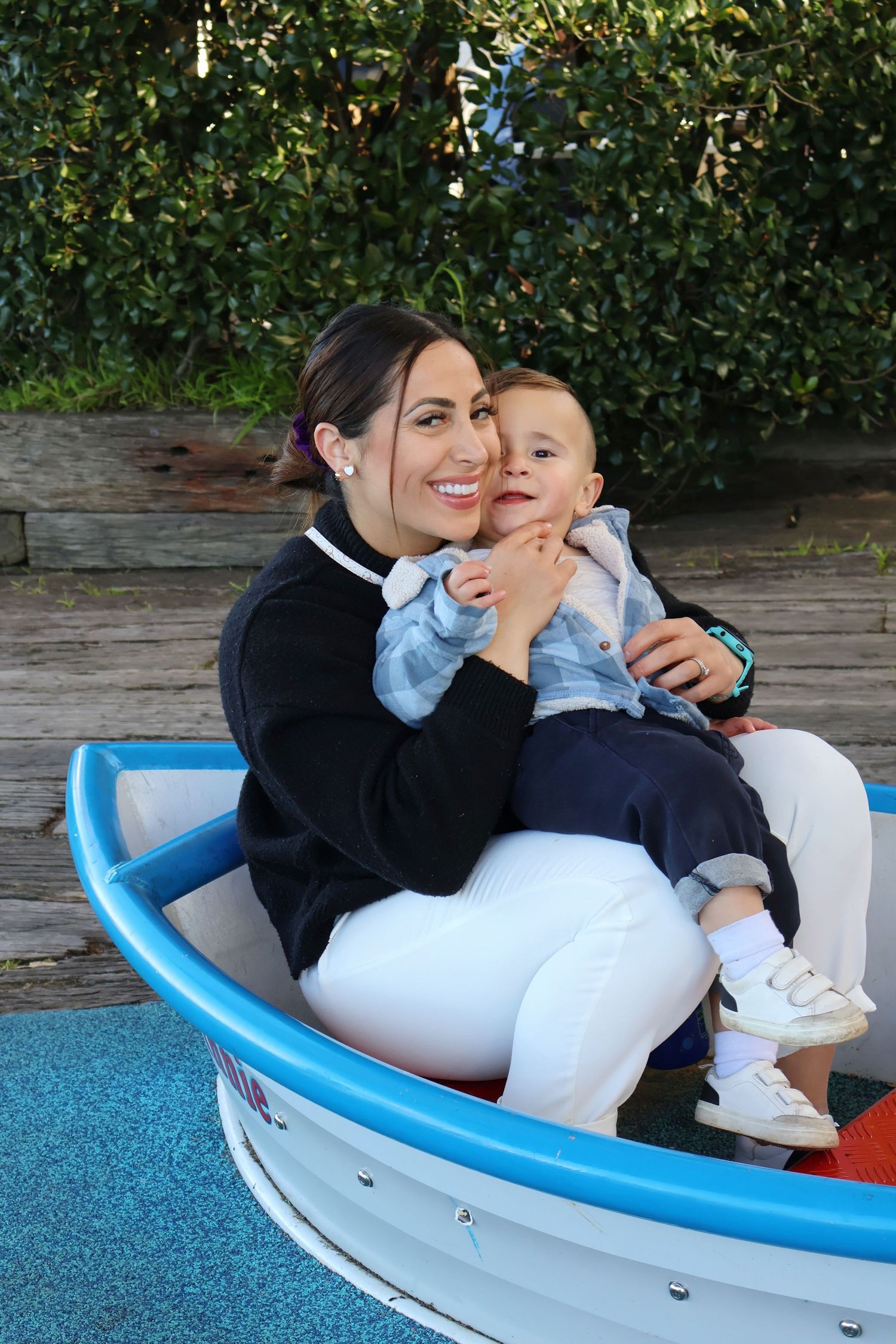 Smiling mother holding happy toddler boy sitting in colorful ride-on boat.