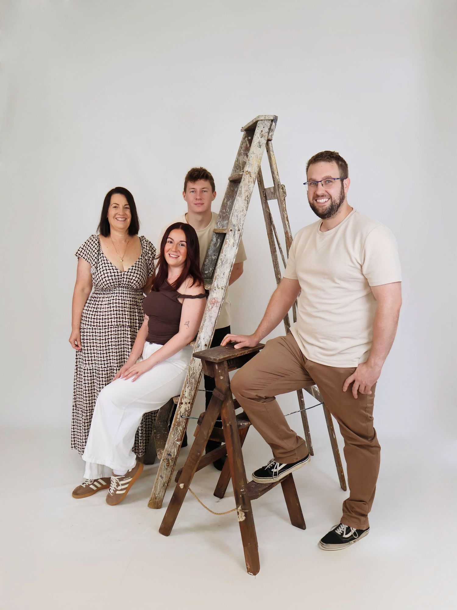 Family of four posing with rustic wooden ladder prop in bright white photography studio.