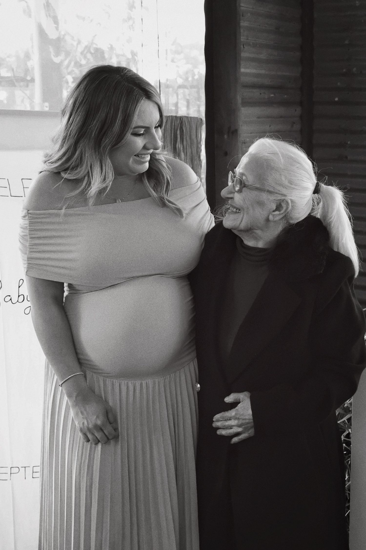 Black and white photo of pregnant woman standing with elderly woman at baby shower.