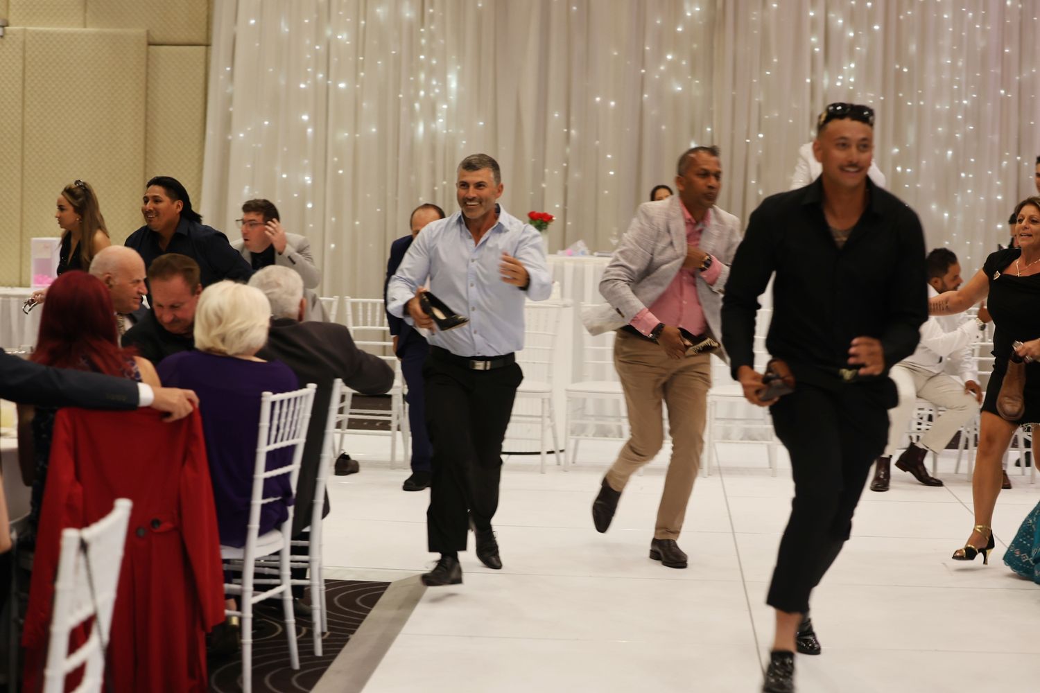 Men running across a wedding reception dance floor in formal attire during a lively celebration.