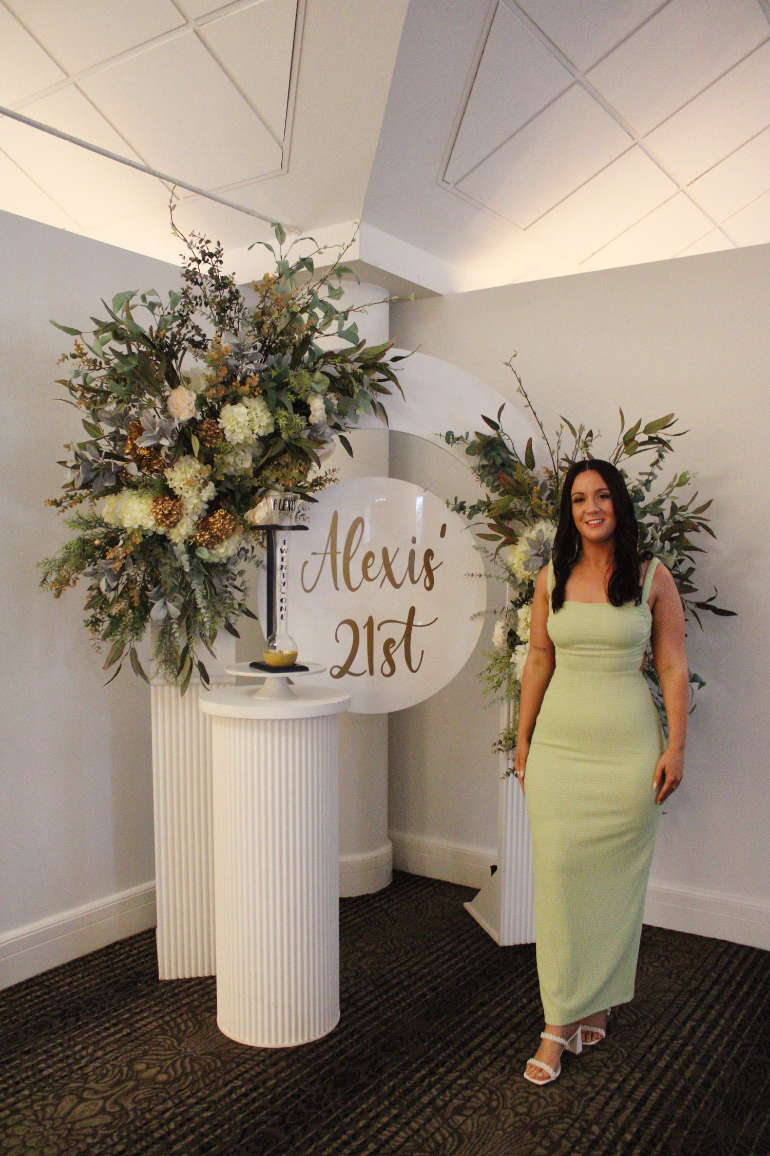 A woman in a mint green dress poses beside floral arrangements at Alexis' 21st birthday celebration.