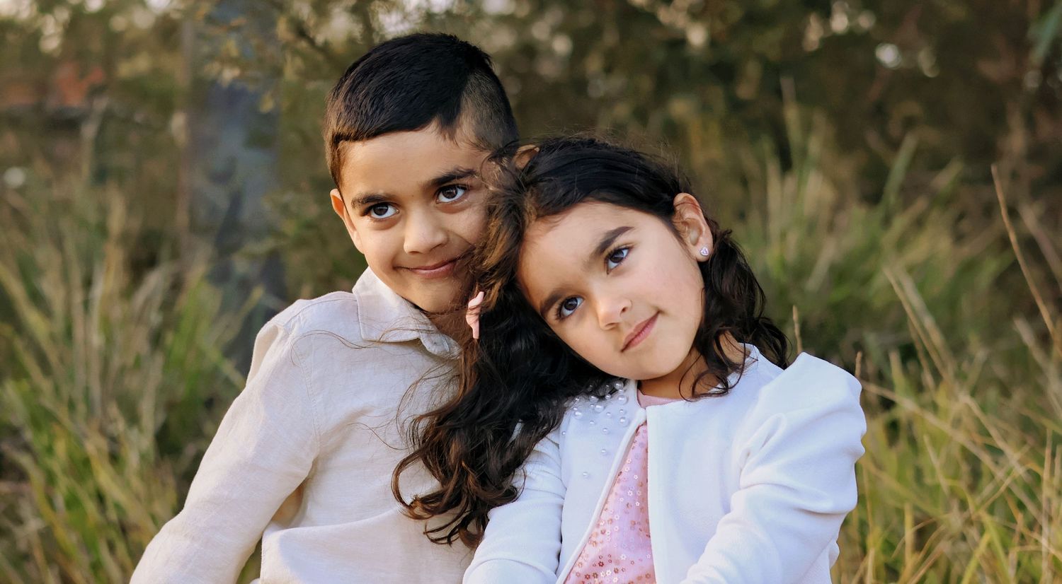 Sweet young brother and sister hugging closely together outdoors in grassy field.