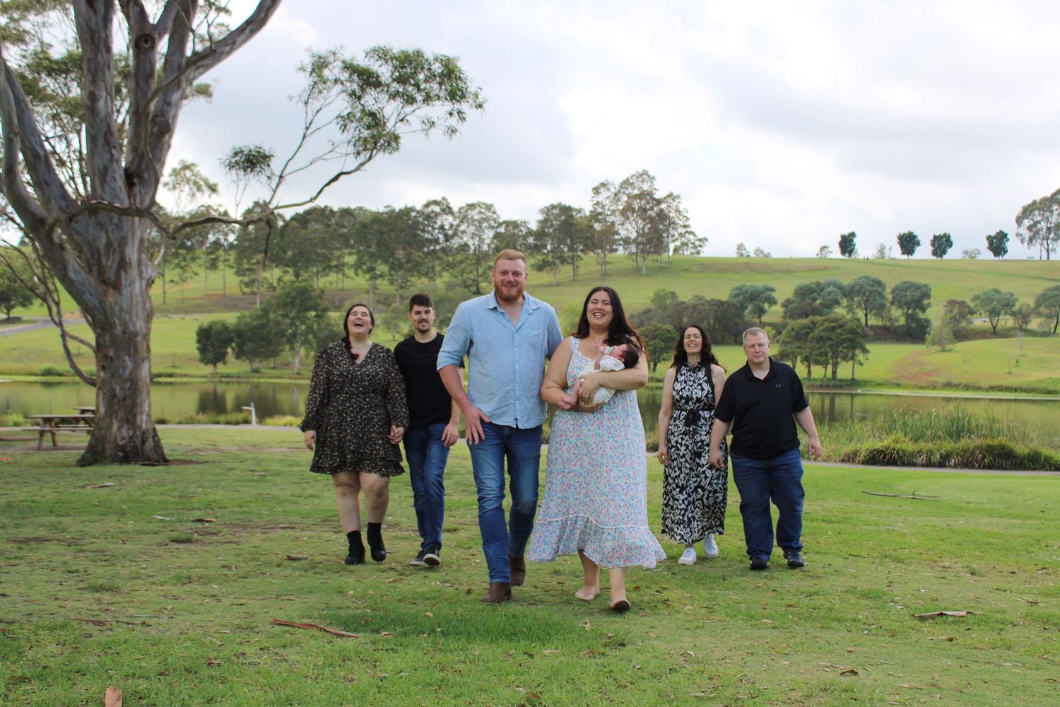 Extended family of six walking together across a scenic green countryside landscape.