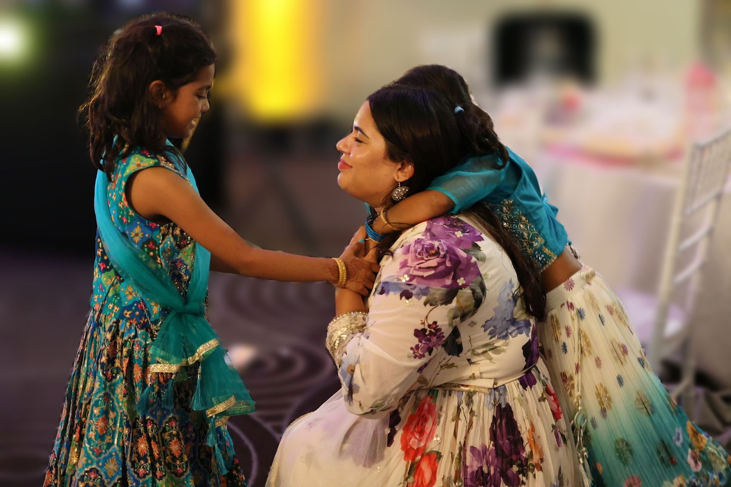 Woman in floral dress sharing a tender moment with two young girls in teal outfits.