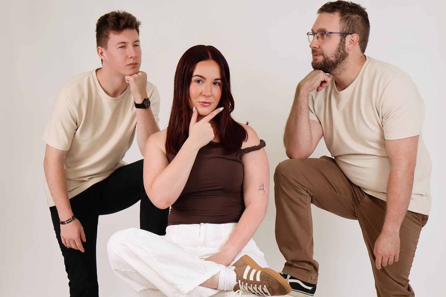 Three friends posing thoughtfully in casual beige and brown outfits against a white studio backdrop.