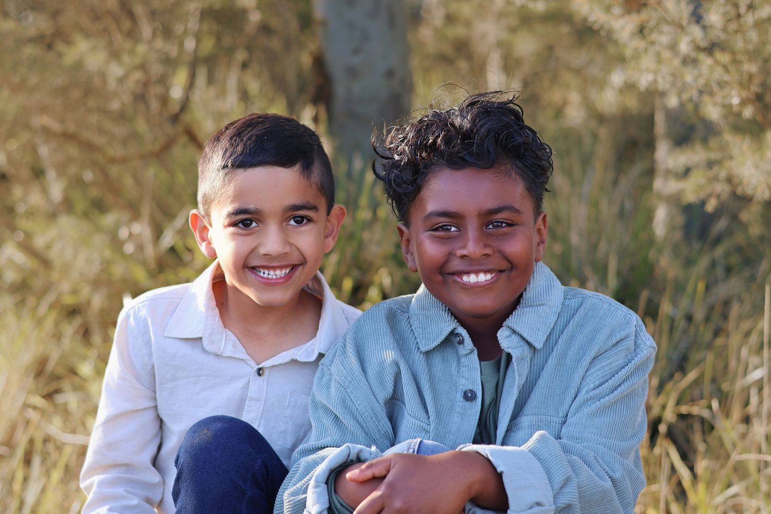 Two smiling young boys sitting together outdoors in golden natural surroundings.