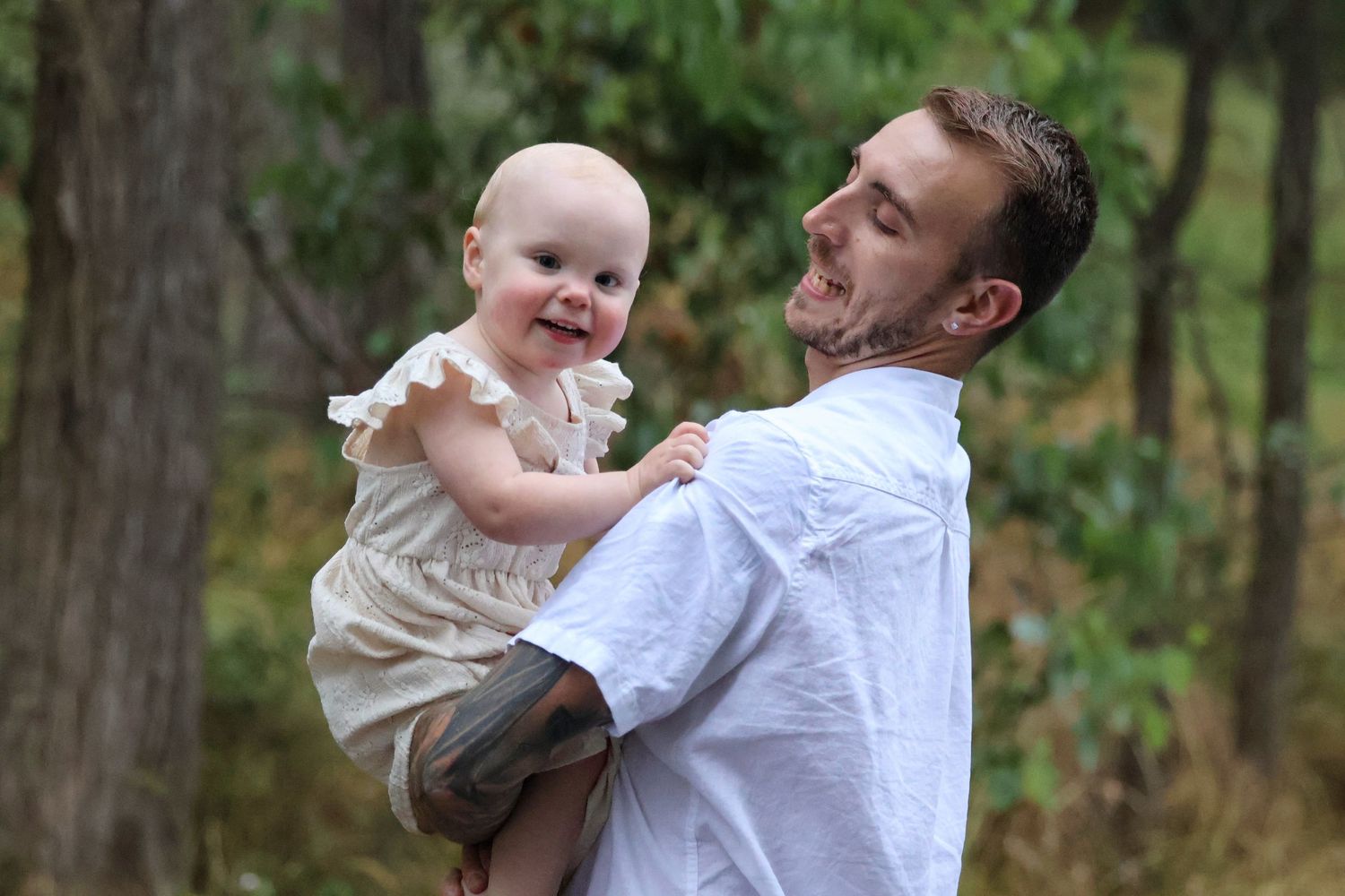 Father holding a smiling baby girl up in a lush outdoor setting during golden hour.