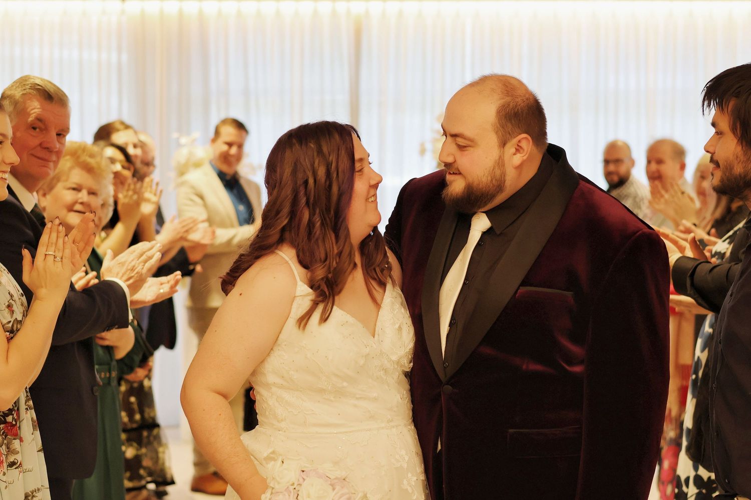 Joyful newlyweds sharing a romantic moment while guests celebrate during wedding reception.