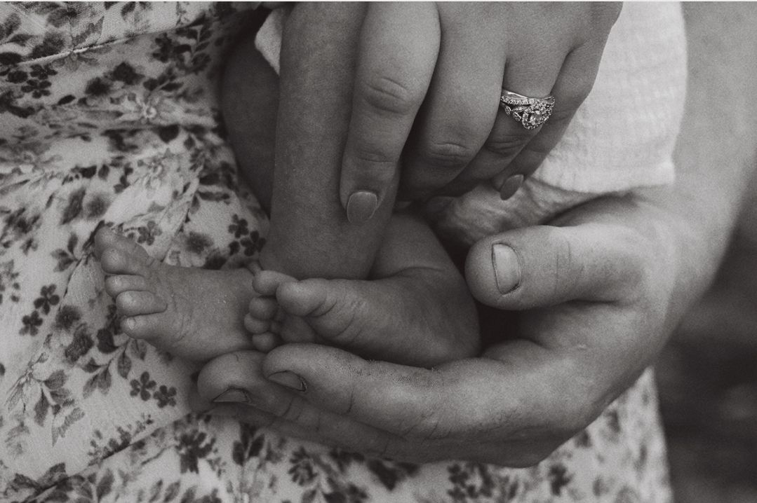 Black and white close-up of adult hands gently cradling a newborn babys tiny feet.