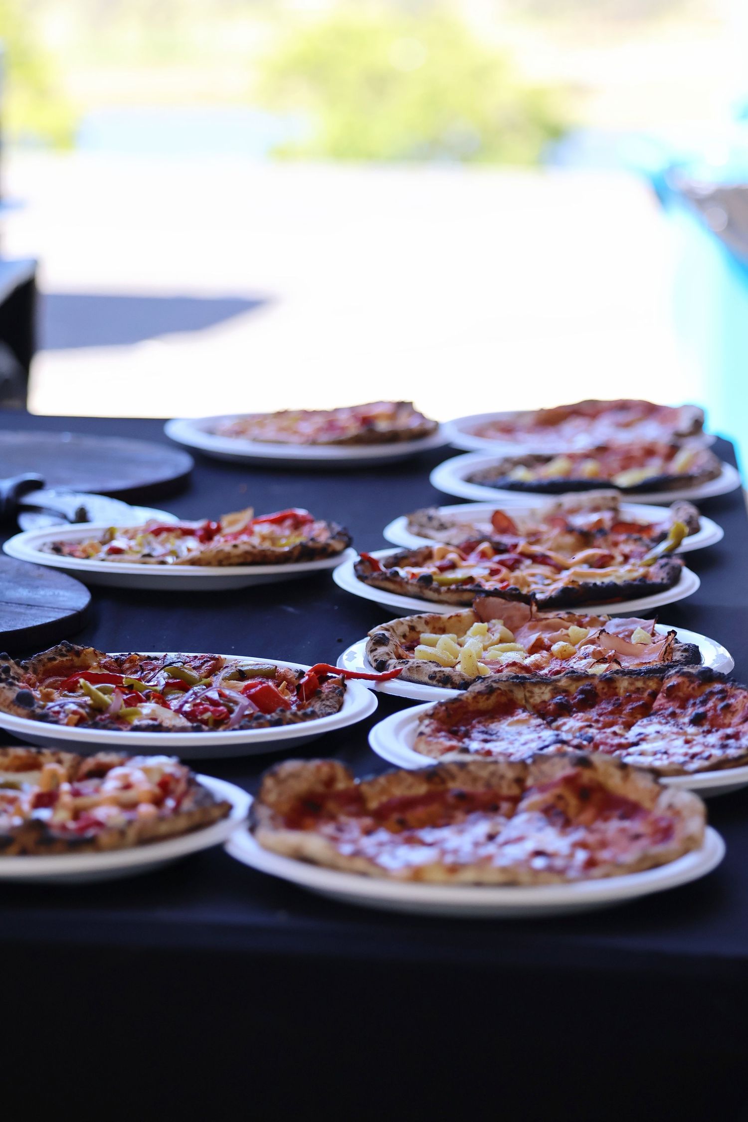 Multiple pizzas on white plates displayed on a black tablecloth at a catering event.