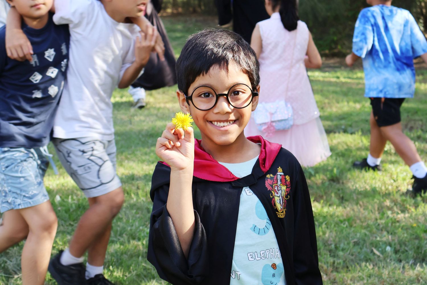 Young boy dressed in Harry Potter costume holding a yellow flower at an outdoor school event.