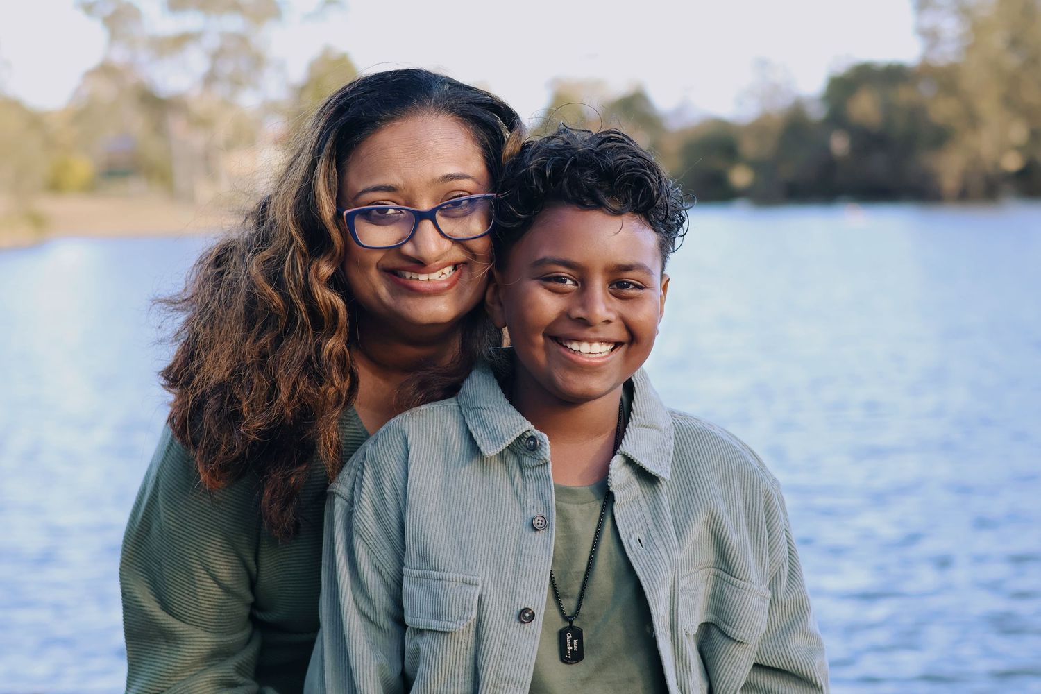 Two smiling women pose together affectionately in front of a beautiful blue lake.