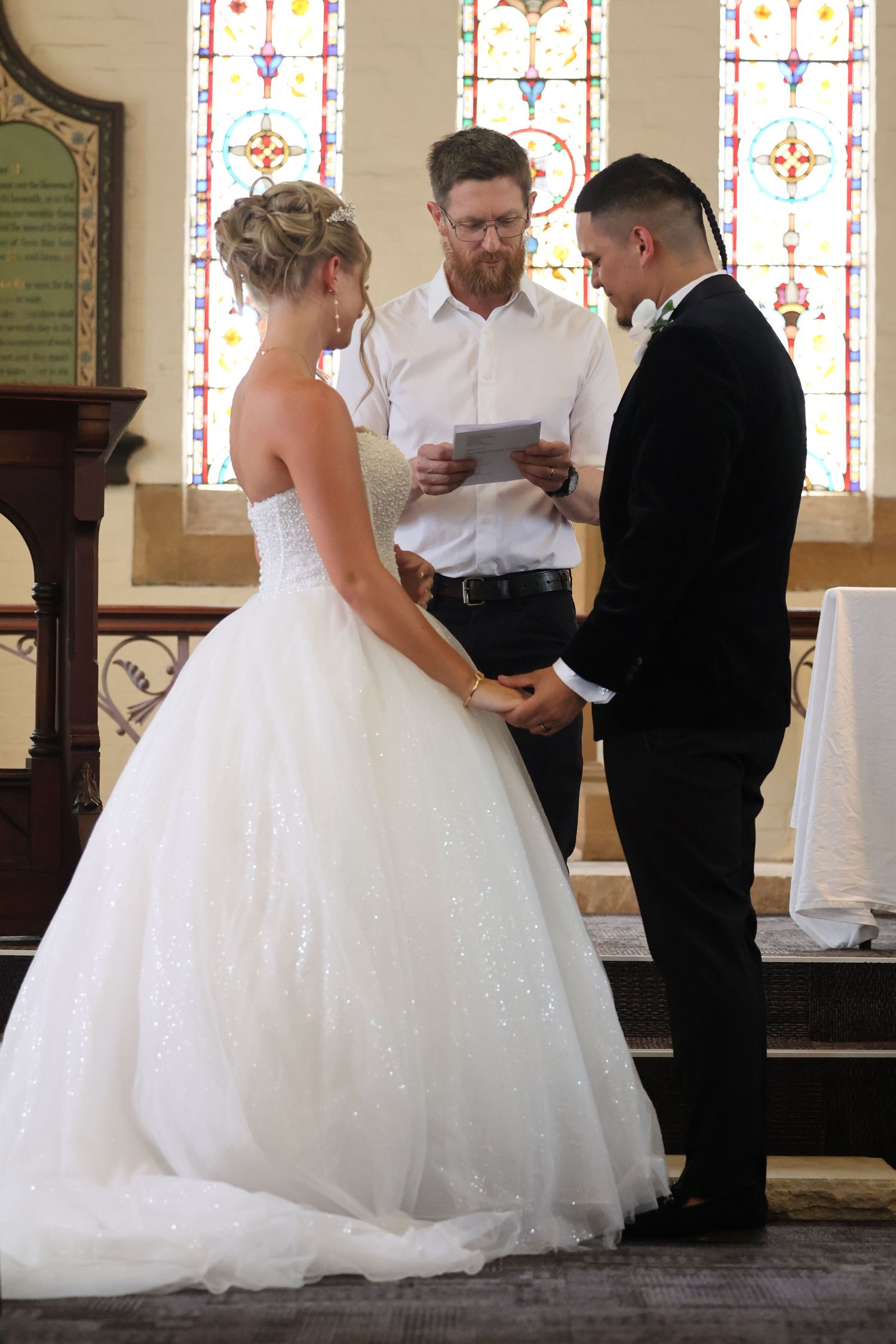 Bride and groom holding hands facing officiant during wedding ceremony in historic church.