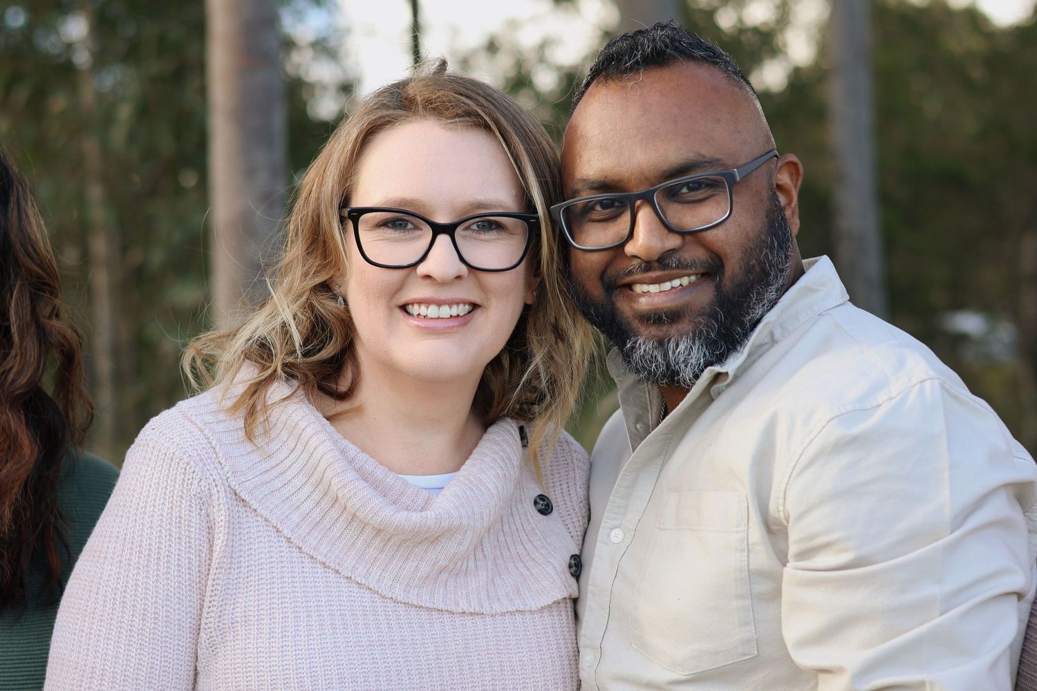 Smiling interracial couple wearing glasses posing together outdoors in soft light.