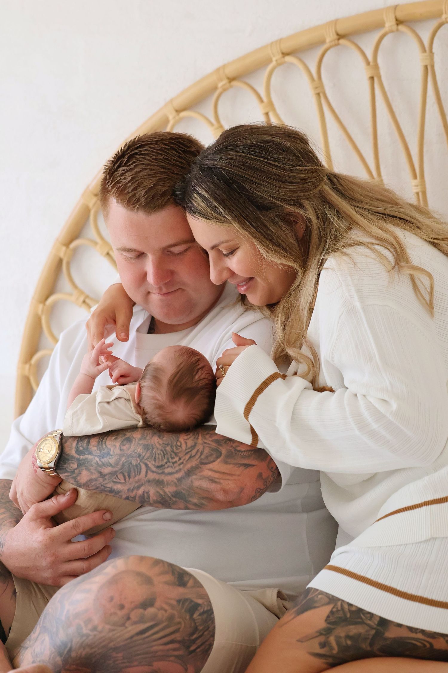 Loving parents with tattoos smiling and bonding with their newborn in a rattan chair.