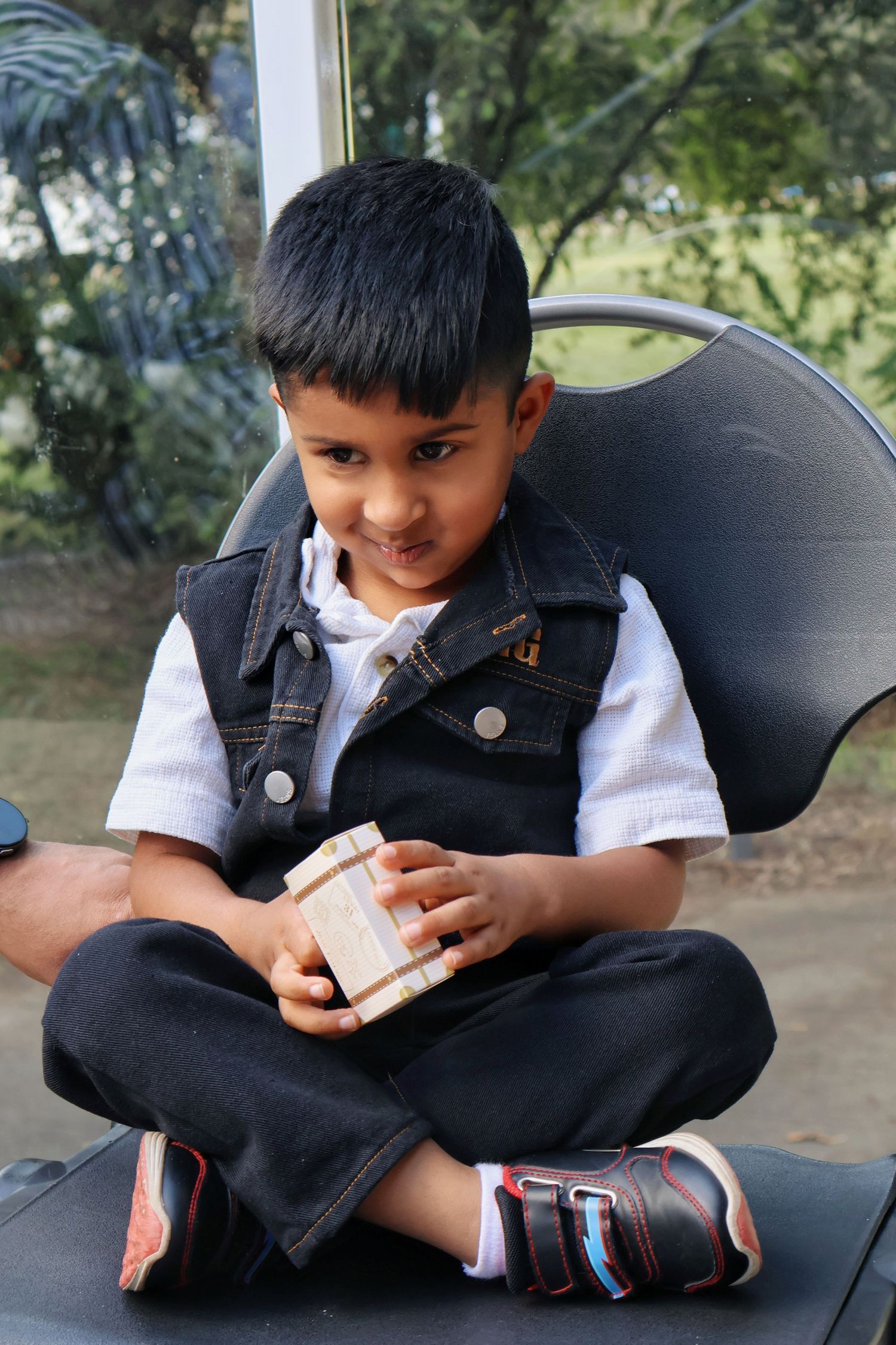A young boy in a denim vest sits cross-legged holding a small wooden gift box.