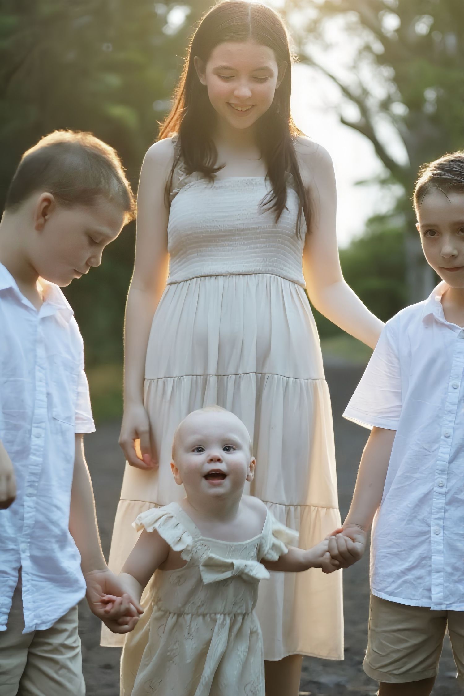 Young mother holding hands with her baby and two sons on a sunlit outdoor path.