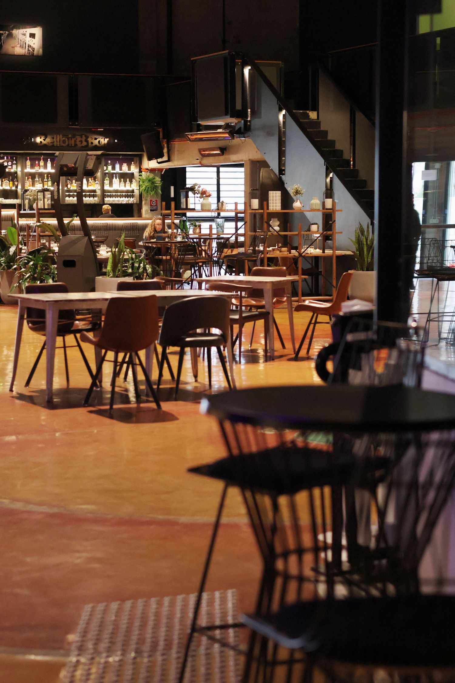 Modern restaurant interior with empty tables, chairs, bar shelves and warm ambient lighting.