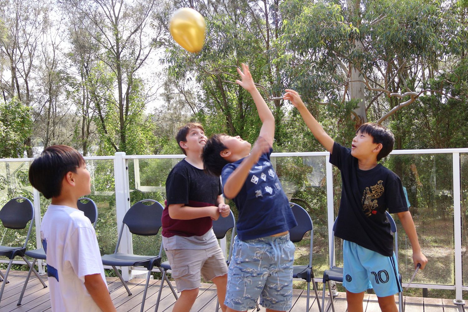 Children playing with a golden balloon snitch outdoors on a wooden deck at a party.