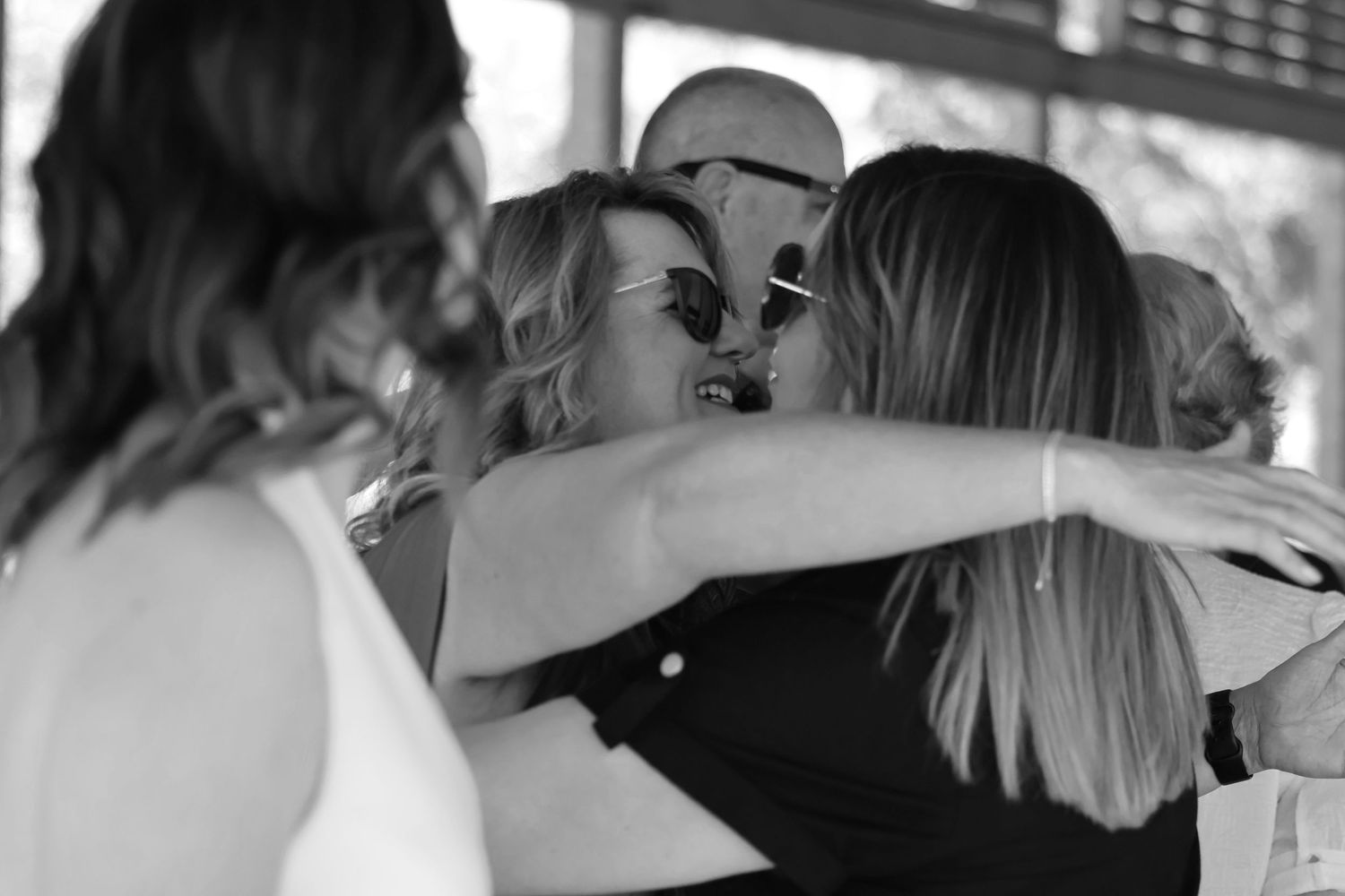Black and white photo of three people sharing a warm group hug at an outdoor gathering.
