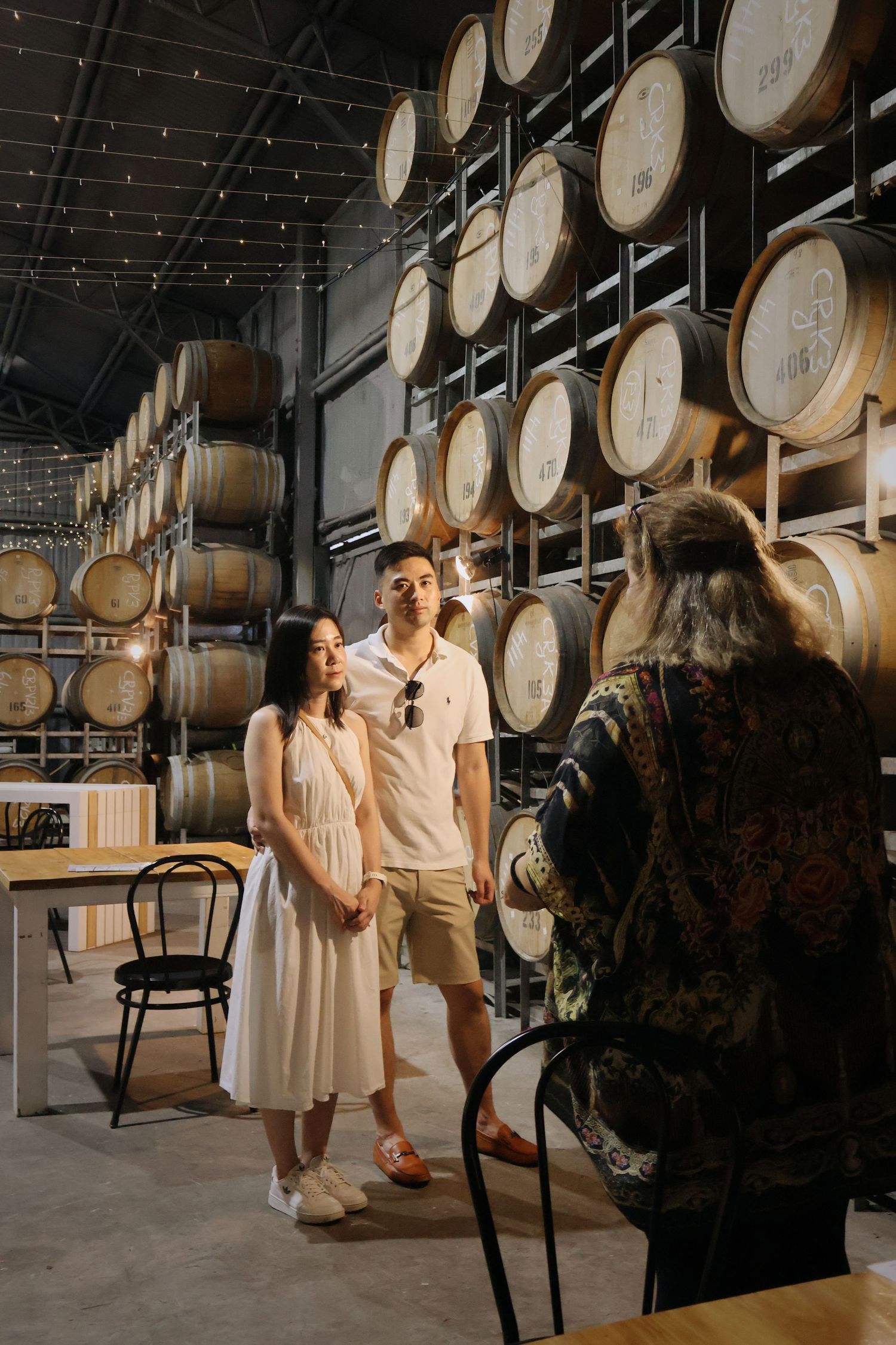 Couple posing for photos in front of wine barrels at a winery cellar door.